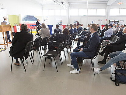 Mehrere Personen sitzen in einer großen Halle und hören einem Vortrag zu